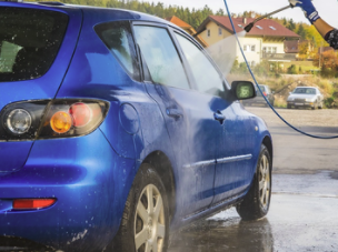 A power washing service in action against a small blue car.
